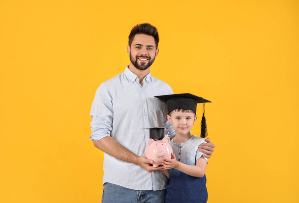 色の背景に貯金箱を持つ小さな男の子と父親。教育のための貯蓄の概念 - 写真・画像
