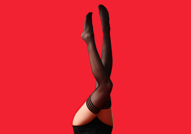 Legs of beautiful young woman in stockings on color background - 写真・画像