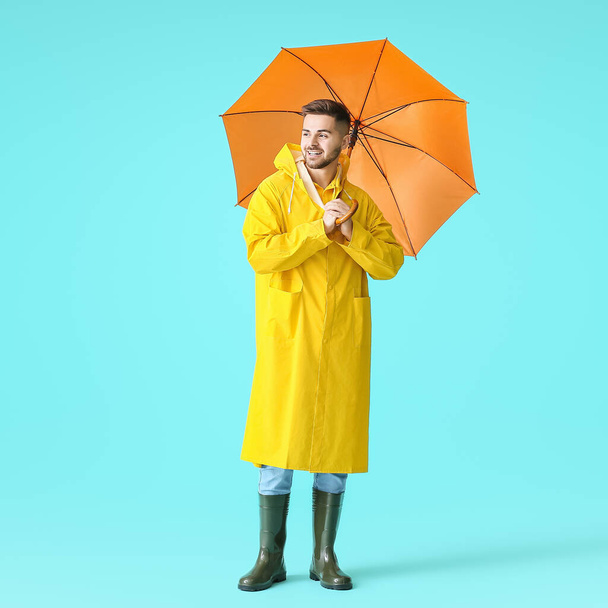 Jovem de capa de chuva e com guarda-chuva sobre fundo de cor
 - Foto, Imagem