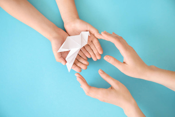 Hands of family with paper dove on color background - Photo, Image