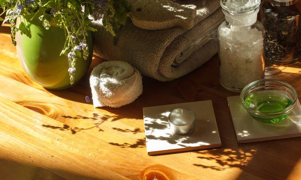 Рушник для ванни, ароматизована сіль, свічки та інші аксесуари для ванни та глечик з квітами на дерев'яному столі, красиві тіні
 - Фото, зображення