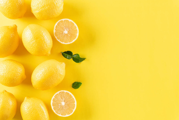 オレンジ、レモン、緑の葉をパステルイエローの背景で作った夏の組成物。果物の最小限の概念。フラットレイアウト、トップビュー、コピースペース. - 写真・画像