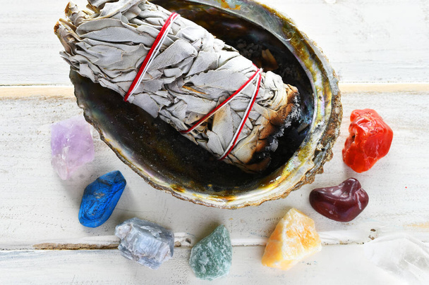 A close up image of Chakra healing crystals with white sage smudge sticks and orange sacred feather.  - Fotó, kép