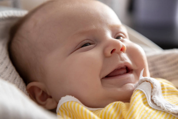 Un ritratto ravvicinato di una bambina che giace a letto e sorride. Una bambina di tre mesi in abiti gialli ride. Foto di alta qualità - Foto, immagini