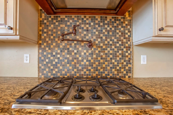 Cooktop and exhaust hood inside kitchen with faucet on the tile backsplash wall - Photo, Image