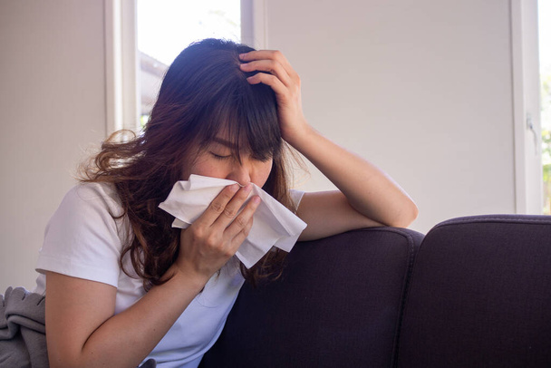 Donna asiatica seduta sul divano all'interno della casa ha la febbre, avendo un panno bocca dopo aver coperto la bocca dopo aver impedito la diffusione COVID-19 si sta diffondendo in tutto il mondo - Foto, immagini