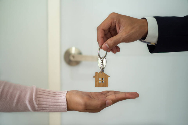 The business man in the suit giving a house key to the woman's hand. Employees sending a new home keys to buyers. concept of Landlords or buying and selling real estate rentals - Photo, Image