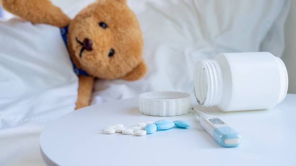 Brown teddy bear is sick in bed depression beside, there was a medicine placed on the table. - Photo, Image