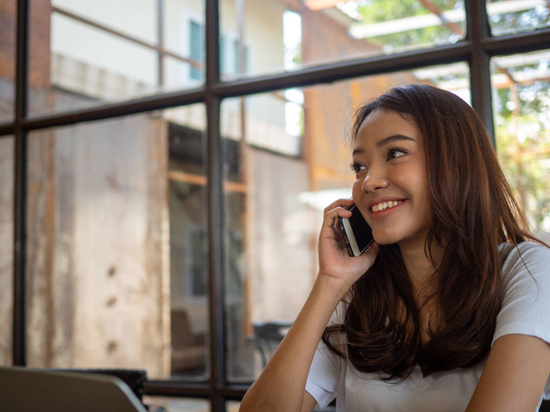 Азиатские девушки счастливы и улыбаются, разговаривая по телефону в кафе
. - Фото, изображение