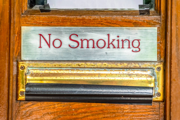 Nenhum sinal de fumar acima da ranhura da gota do correio com fita preta contra a porta marrom da madeira
 - Foto, Imagem