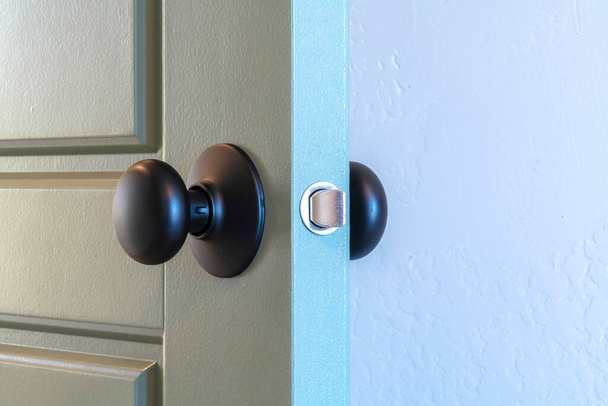 Cierre de una perilla de puerta negra redonda instalada en una puerta interior con paneles grises
 - Foto, Imagen