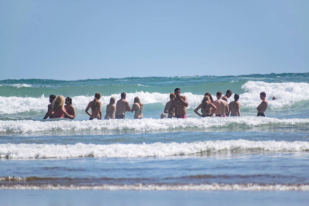 Окленд / Нова Зеландія - 31 січня 2020: Група людей, чоловіків і жінок у плавальному одязі відходи глибоко в океанічних хвилях на пляжі Піха. - Фото, зображення