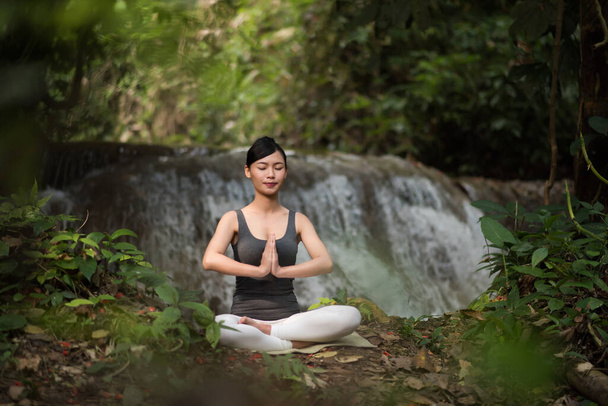 Young woman in yoga pose sitting near waterfall - Fotoğraf, Görsel