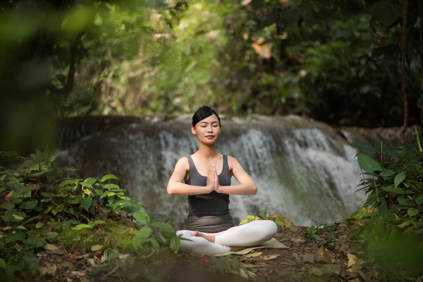 Yoga yapan genç bir kadın şelalenin yanında oturuyor. - Fotoğraf, Görsel