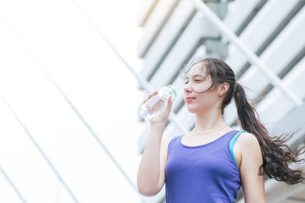 現代の都市で運動を実行している女性飲料水ボトルは、外のウェルネススポーツウェアを着用してください。若い女性は明るい日当たりの良い外で運動屋外ワークアウト。健康的なウェルネスライフスタイルの女性のコンセプト - 写真・画像