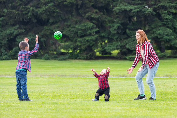 Bonne jeune mère joue avec le ballon avec son bébé dans un parc sur une pelouse verdoyante.Concept d'une famille heureuse. La fête des mères. Mère et fils ont des activités ensemble pendant les vacances
. - Photo, image