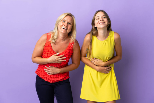 Mom and daughter isolated on purple background smiling a lot while putting hands on chest - Photo, Image