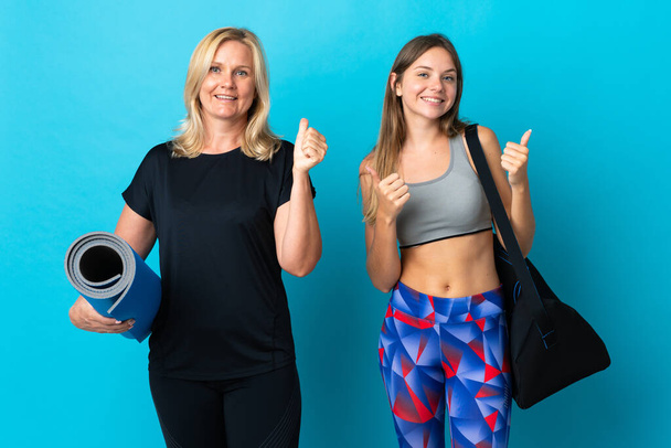 Mom and daughter doing yoga isolated on blue background giving a thumbs up gesture with both hands and smiling - Foto, imagen