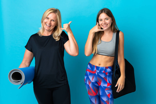 Mutter und Tochter machen isoliert Yoga auf blauem Hintergrund und machen Handygesten. Rufen Sie mich zurück - Foto, Bild