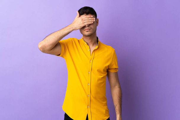 手で目を覆う紫色の背景に隔離された若いコロンビア人男性。何か見たくない - 写真・画像