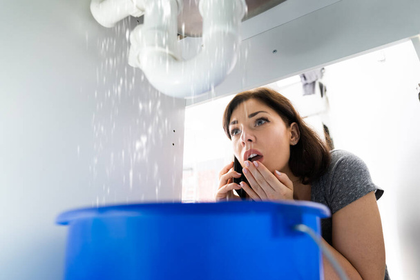 Women Doing Emergency Plumber Phone Call In Kitchen At Home - 写真・画像