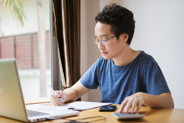 Young Asian businessman in relax casual during working from home. Asian man staying at home and setup a small workplace during COVID-19 self isolation. Work from home concept during coronavirus crisis - Foto, imagen