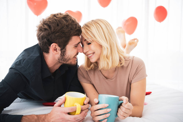 Lovely caucasian young couple enjoying breakfast set on the bed in bedroom together. Caucasian couple's portrait in relaxation posing. - Photo, Image