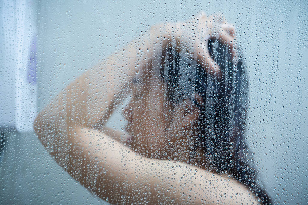 Beautiful Asian woman enjoy taking a shower in the shower room with a drops of water on glass. - Foto, afbeelding
