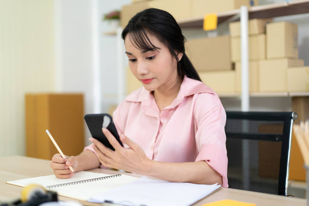 Beautiful Asian woman's portrait in e-commerce and online shopping concept, woman writing a note on notebook. - Photo, image
