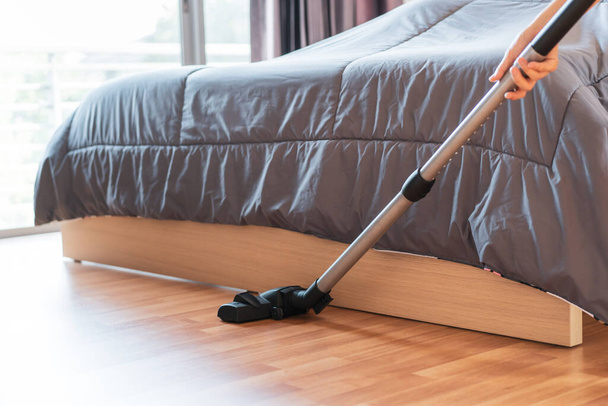 Woman cleaning the bedroom in her house by using a vacuum to clean up a wooden floor. Routine housework in everyday life concept with copyspace. - Fotoğraf, Görsel
