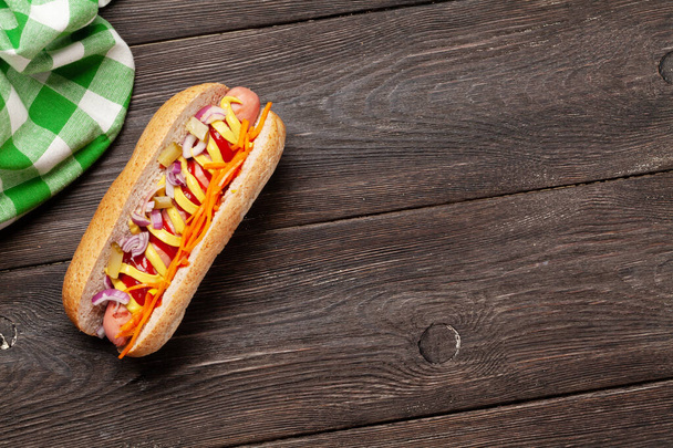 Cachorro quente com legumes e condimentos em fundo de madeira. Vista superior com espaço de cópia. Depósito plano
 - Foto, Imagem