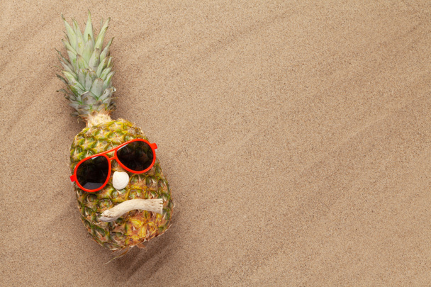 Ripe pineapple with sunglasses over hot sand beach with copy space. Travel and vacation concept. Top view flat lay - Photo, Image