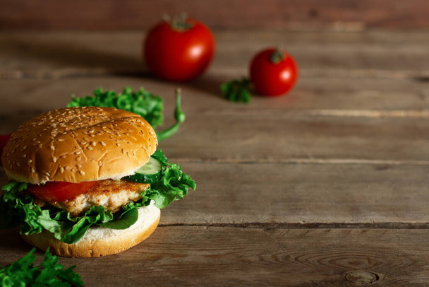 Fresh tasty chicken burger, tomato and lettuce on a wooden table. - Foto, afbeelding