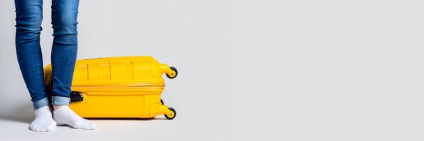 Yellow suitcase and female legs on a light background. Vacation and travel concept. Banner. - Fotoğraf, Görsel