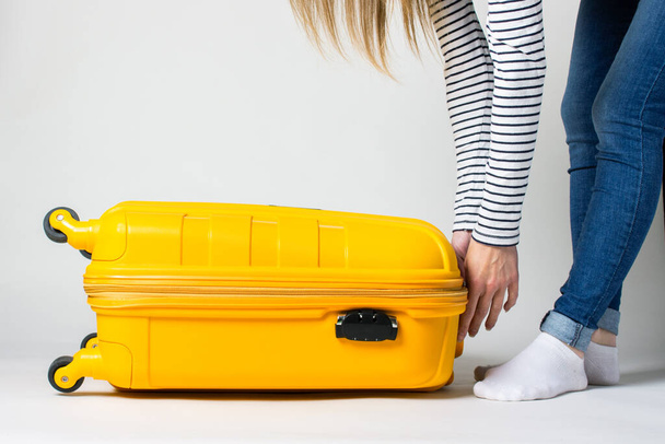 Jonge vrouw sluit een koffer op een lichte achtergrond. Vakantie en reizen concept. - Foto, afbeelding