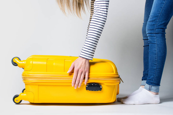 Jonge vrouw opent een koffer op een lichte achtergrond. Vakantie en reizen concept. - Foto, afbeelding