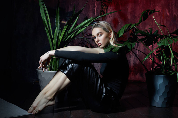Fashion woman sitting on the floor in tropical foliage pink light. Wet hair, perfect figure and makeup. Beautiful blonde girl and monster leaves - Fotó, kép