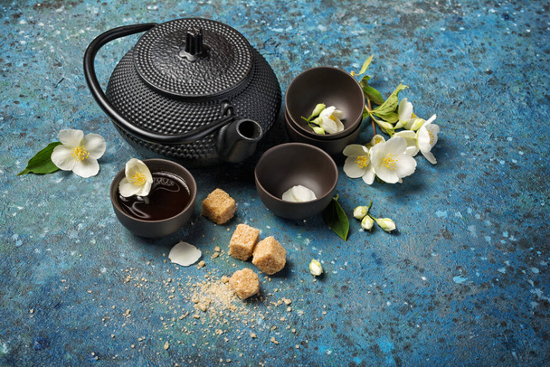 Bouilloire traditionnelle noire orientale et tasses avec thé au jasmin vert sain avec canne ou sucre brun sur fond de béton bleu avec espace de copie - Photo, image