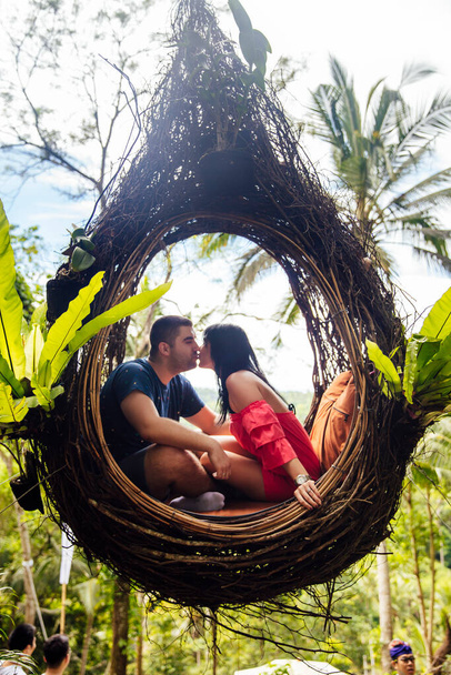 A tourist couple sitting on a large bird nest on a tree at Bali island, Indonesia - Fotó, kép