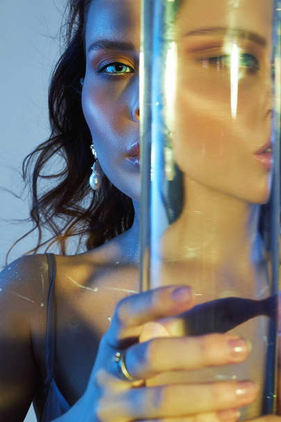 Beauty portrait of a woman with a large glass near her face. Distortion and refraction of reflection through water - Photo, image