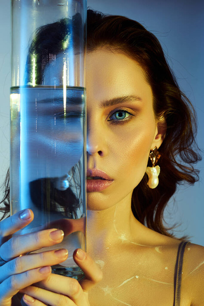 Beauty portrait of a woman with a large glass near her face. Distortion and refraction of reflection through water - Fotoğraf, Görsel