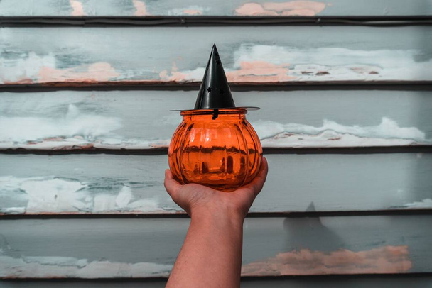 A horizontal shot of a person holding a pumpkin-shaped candle holder with a black top shaped like a hat - Foto, Bild