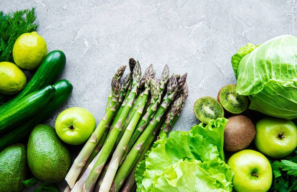 Gezonde vegetarische voeding concept achtergrond, verse groene voeding selectie voor detox dieet, appel, komkommer, asperges, avocado, limoen, salade bovenaanzicht op een concrete achtergrond - Foto, afbeelding