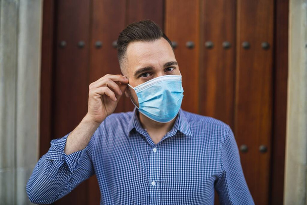 A young male wearing a blue shirt standing at the gate with a medical face mask - Covid-19 global pandemic concept - Photo, Image