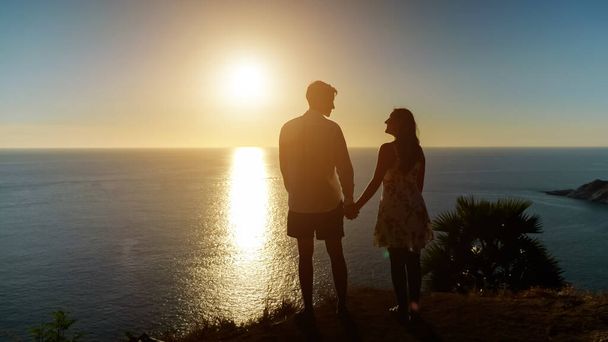 ζευγάρι κρατώντας τα χέρια πηγαίνει στην άκρη άποψη στο υπέροχο ηλιοβασίλεμα - Φωτογραφία, εικόνα
