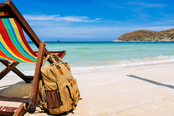 A place for the traveler, freelancer. A deck chair on the sandy shore of a tropical beach overlooking the open sea. a stylish brown backpack standing nearby. The concept of remote work, recreation - Photo, image