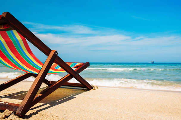 Deck chair on the sandy beach by the sea. The bruise color of the water and the blue sky with broken clouds in the background. A place for relaxation and freelance work. Open sea view with boats on the horizon - Фото, изображение