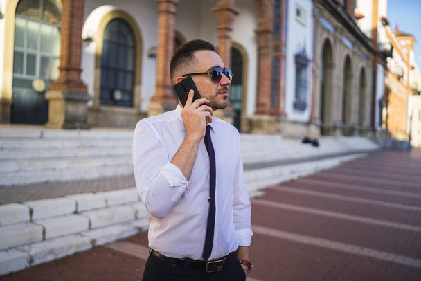 A successful young businessman in a formal outfit with sunglasses talking on the phone - Zdjęcie, obraz