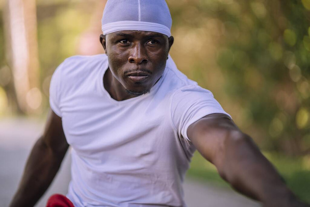 A closeup shot of an African-American male in a white shirt stretching at the park - Photo, image