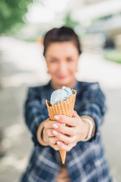 Ένα κορίτσι κρατάει ένα παγωτό χωνάκι στα χέρια της. Παγωτό σε κοντινό πλάνο στο επίκεντρο. Κατακόρυφος προσανατολισμός - Φωτογραφία, εικόνα